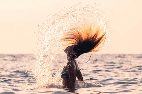 Donna in mare che getta indietro i capelli bagnati sollevando un ventaglio di gocce, al tramonto
