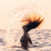Donna in mare che getta indietro i capelli bagnati sollevando un ventaglio di gocce, al tramonto